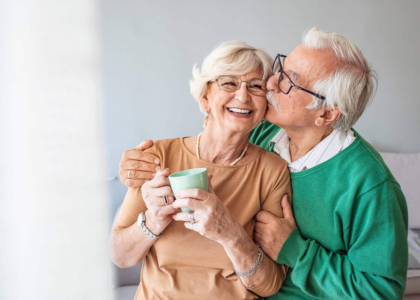husband kissing wife's cheek while she smiles and holds her coffee cup