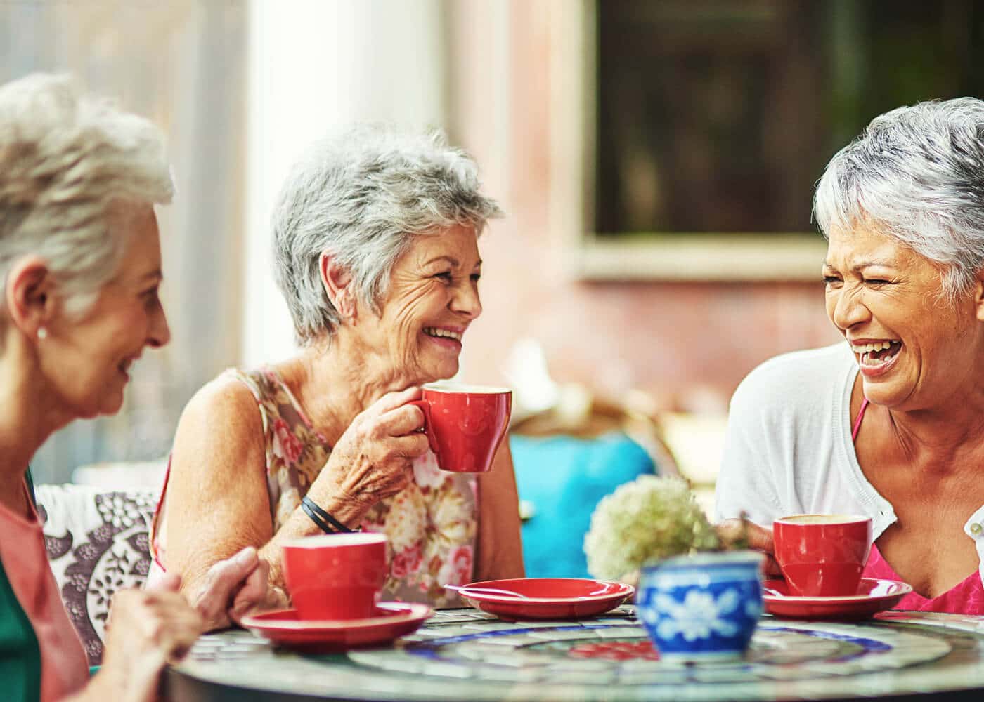 three older ladies laughing and talking over a cup of coffee
