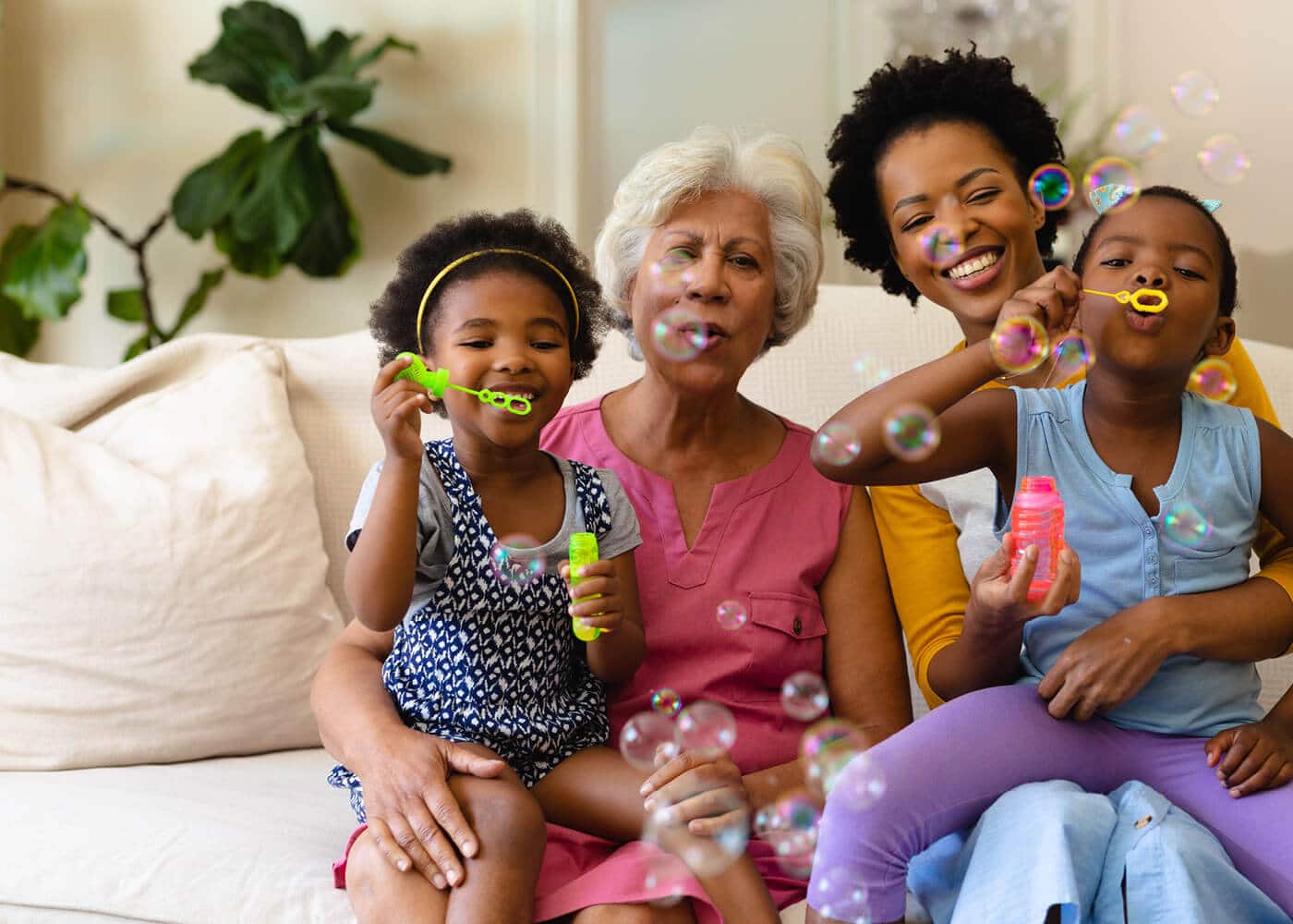 grandma and mom smiling and laughing while granddaughters blow bubbles