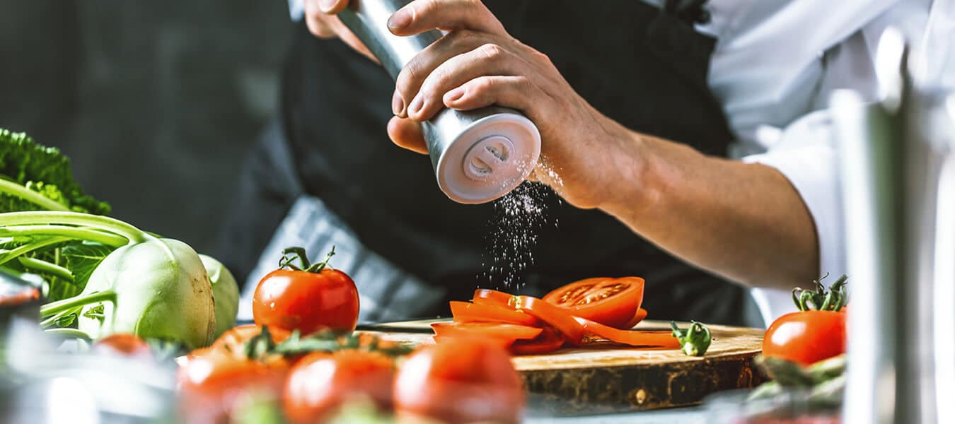 chef grinding salt over a fresh cut tomato